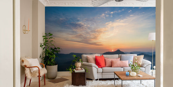 Landscape wall mural featuring a golden sun setting over dark mountain ridges.