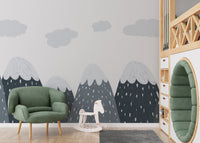 Nursery wall mural with cloud patterns and mountains next to a green velvet chair.