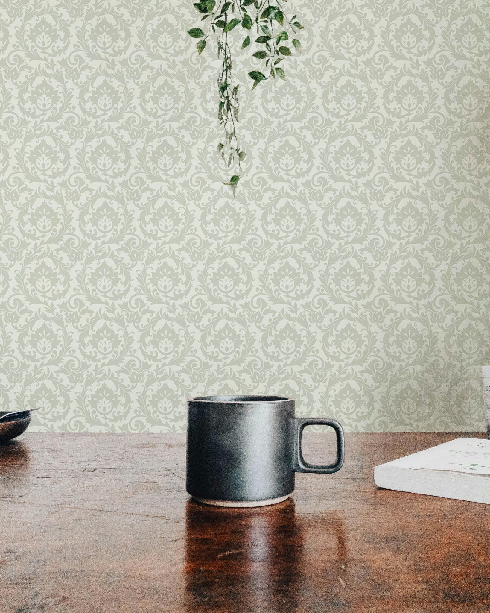 Sage green damask wallpaper backdrop for dark mug on a wooden tabletop