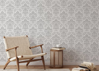 Grey and white damask wallpaper in a reading area with a wooden chair and side table.