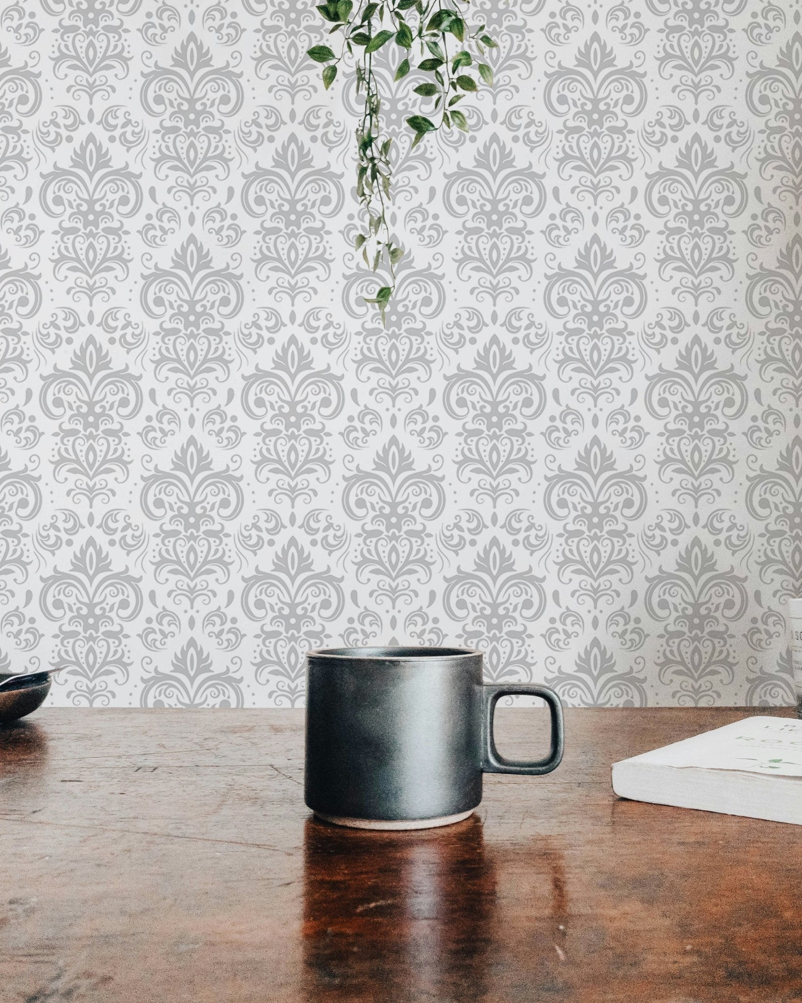 Coffee mug on a wooden table with a blurred white damask wallpaper background.