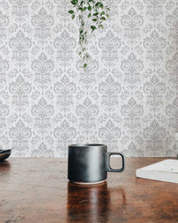 Coffee mug on a wooden table with a blurred white damask wallpaper background.