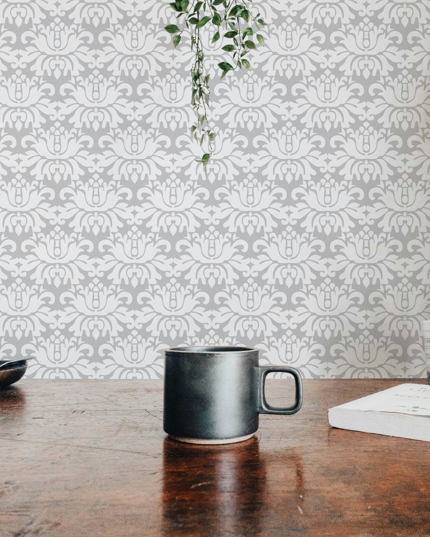 Symmetrical damask wallpaper behind a wooden table with a black ceramic mug.
