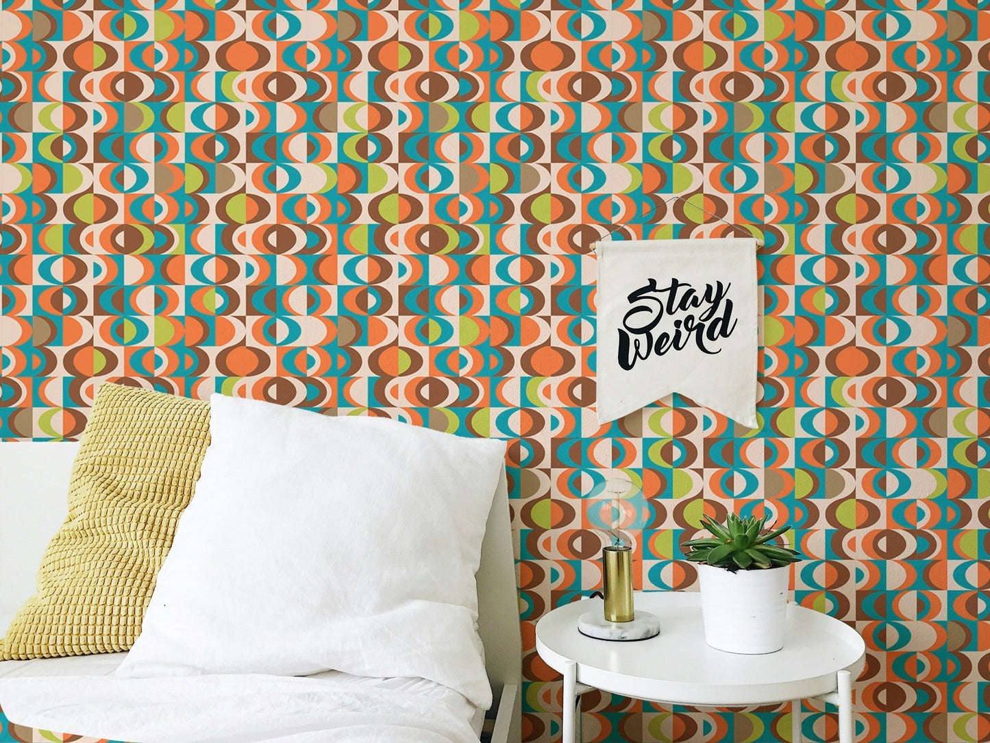 Abstract retro wall mural pattern behind a white bed with a yellow cushion.
