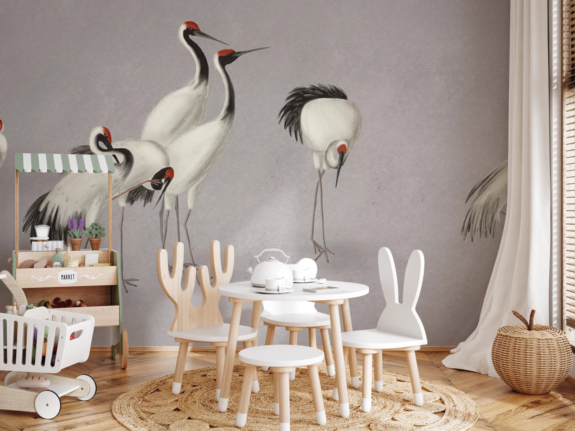 Small activity area for children with cranes print wall mural and white chairs.