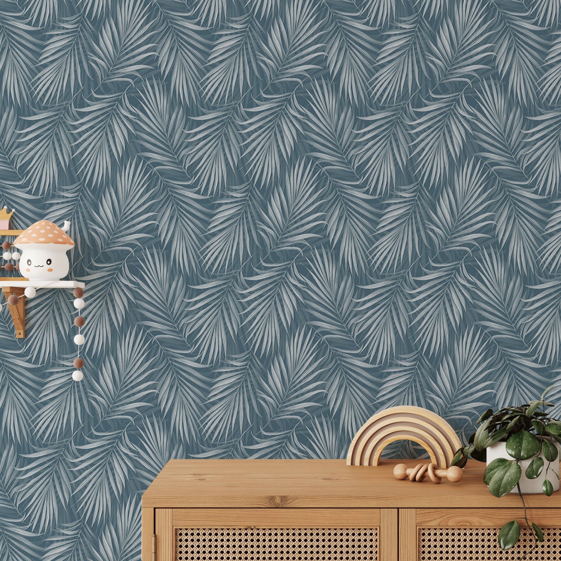 Blue and grey palm leaf wallpaper above a wooden sideboard with nursery decor.