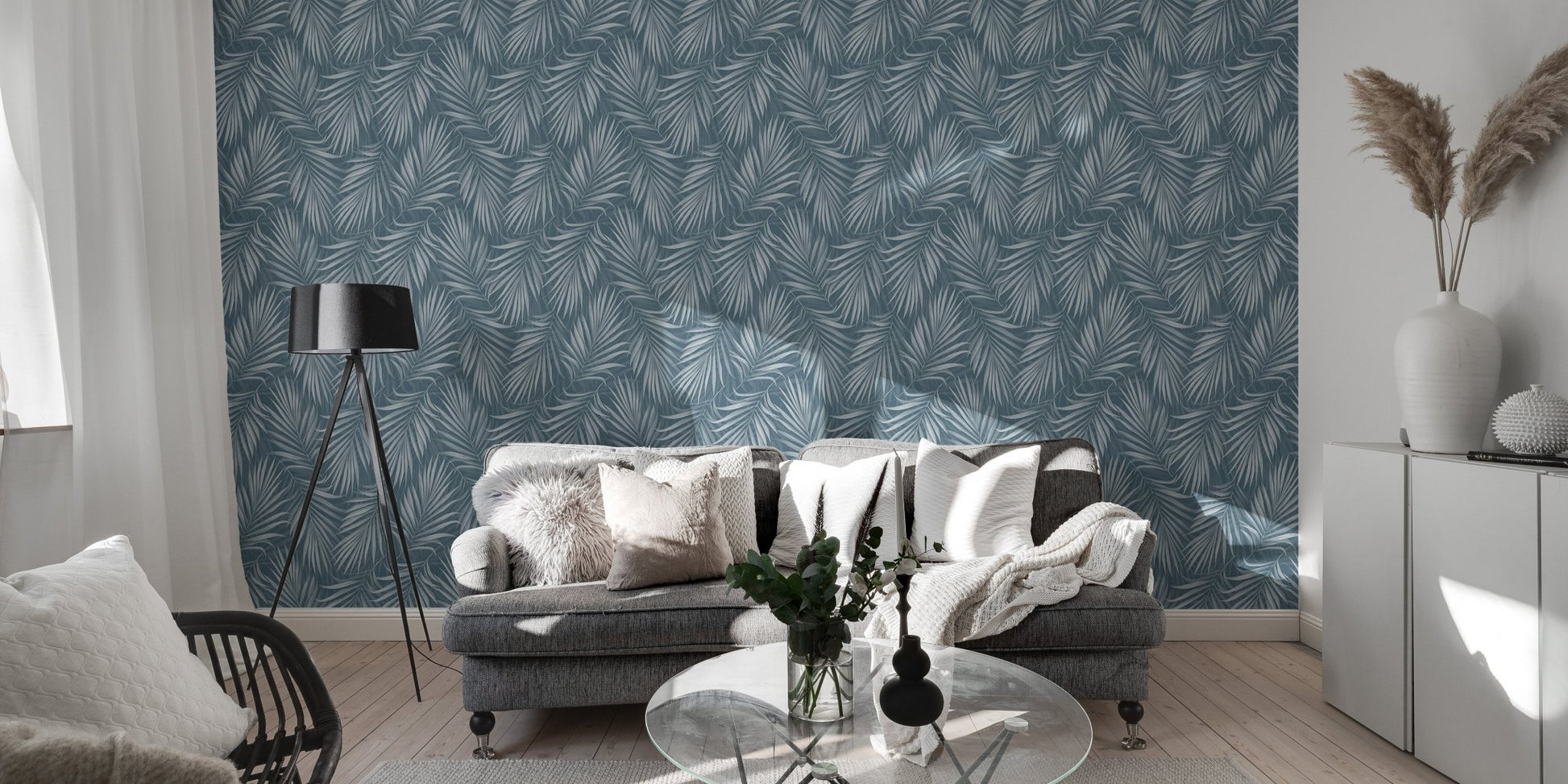 Living area with a grey sofa and a blue tropical leaf wallpaper.