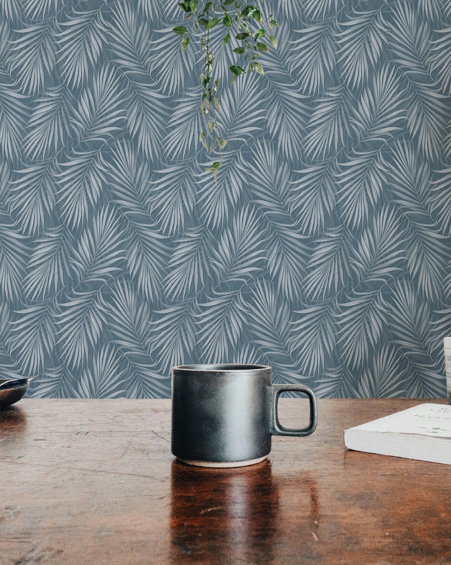 Workspace view with a black mug and a blue tropical leaf wallpaper background.