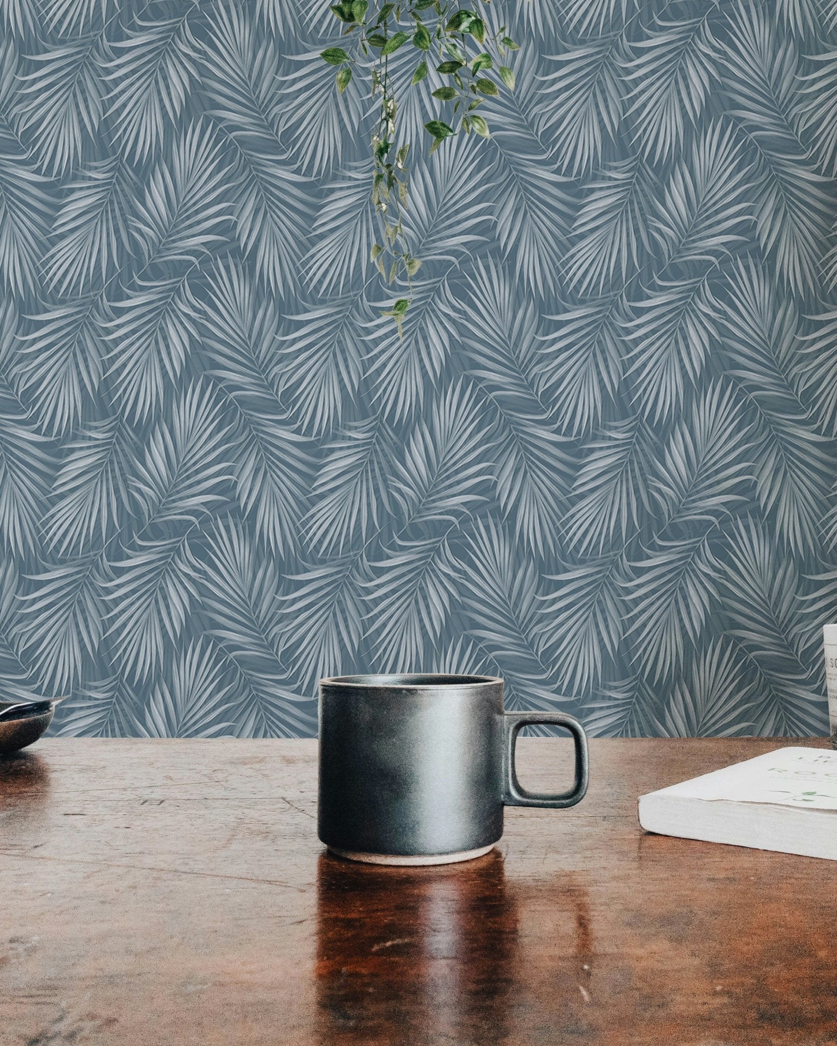 Workspace view with a black mug and a blue tropical leaf wallpaper background.