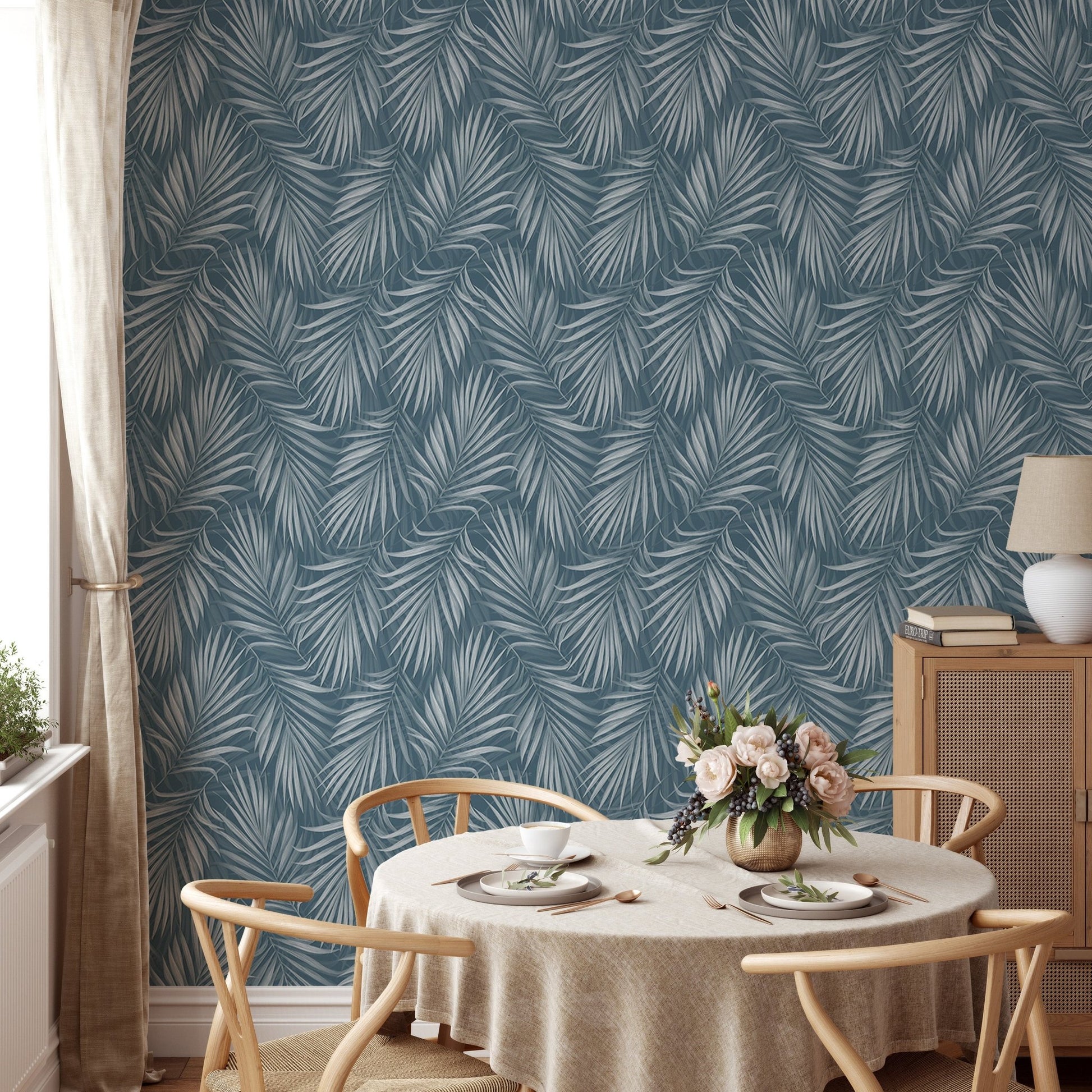 Dining table with wooden chairs against a blue vintage botanical wallpaper.