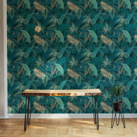 Teal palm leaf wallpaper in room with  wooden side table.