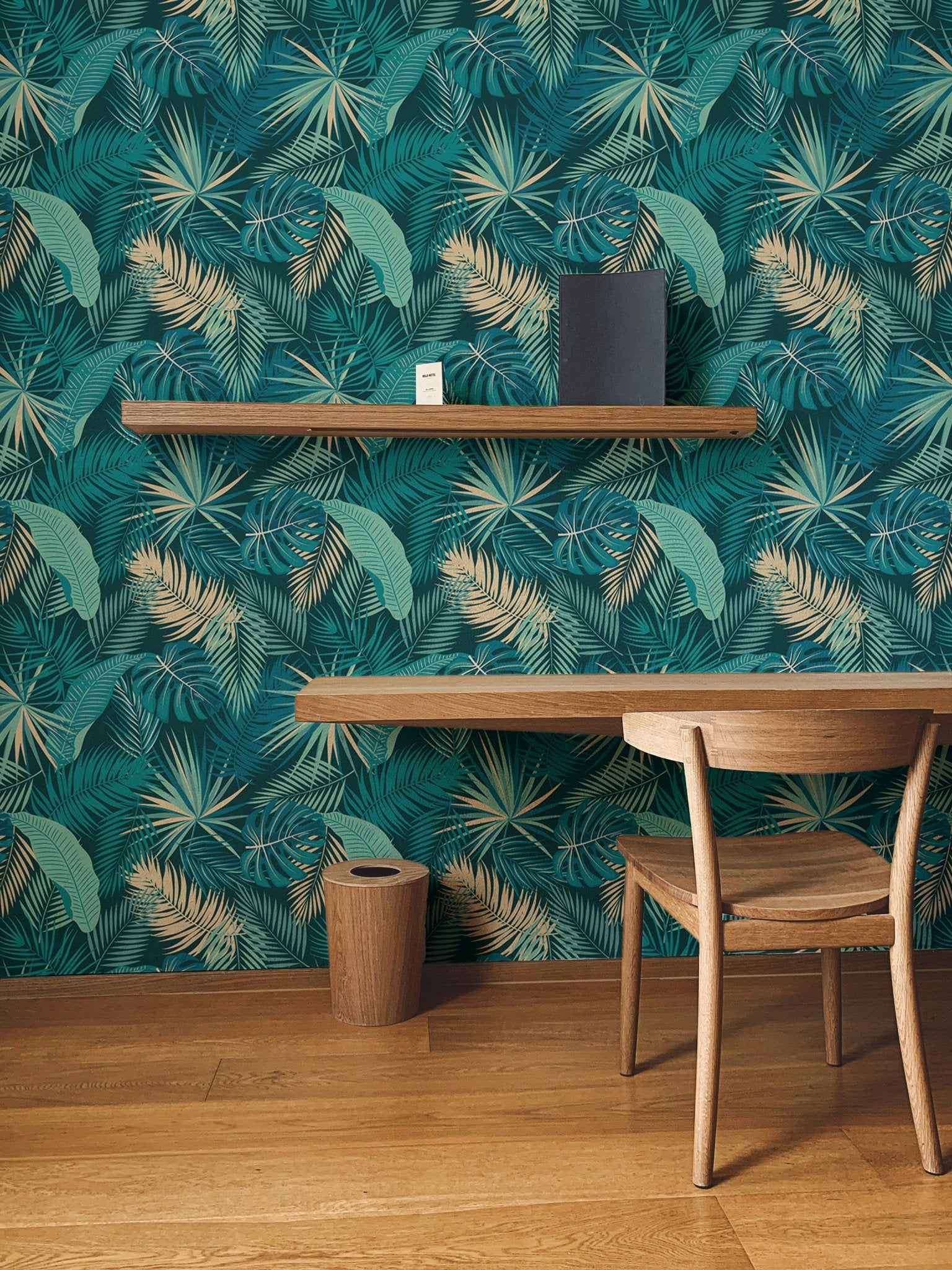 Palm leaves wallpaper on study area wall next to wooden crib and chair.