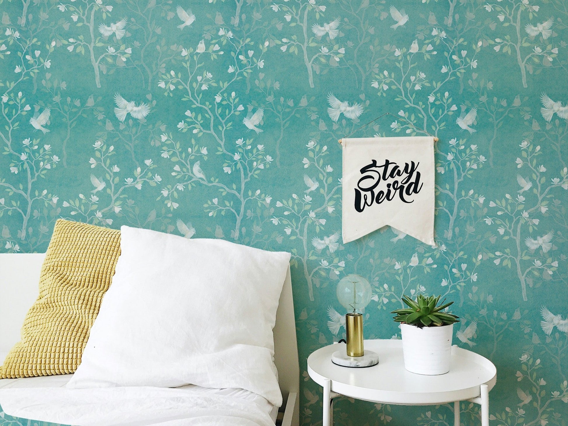 White tree wallpaper on a turquoise background in a minimalist bedroom.
