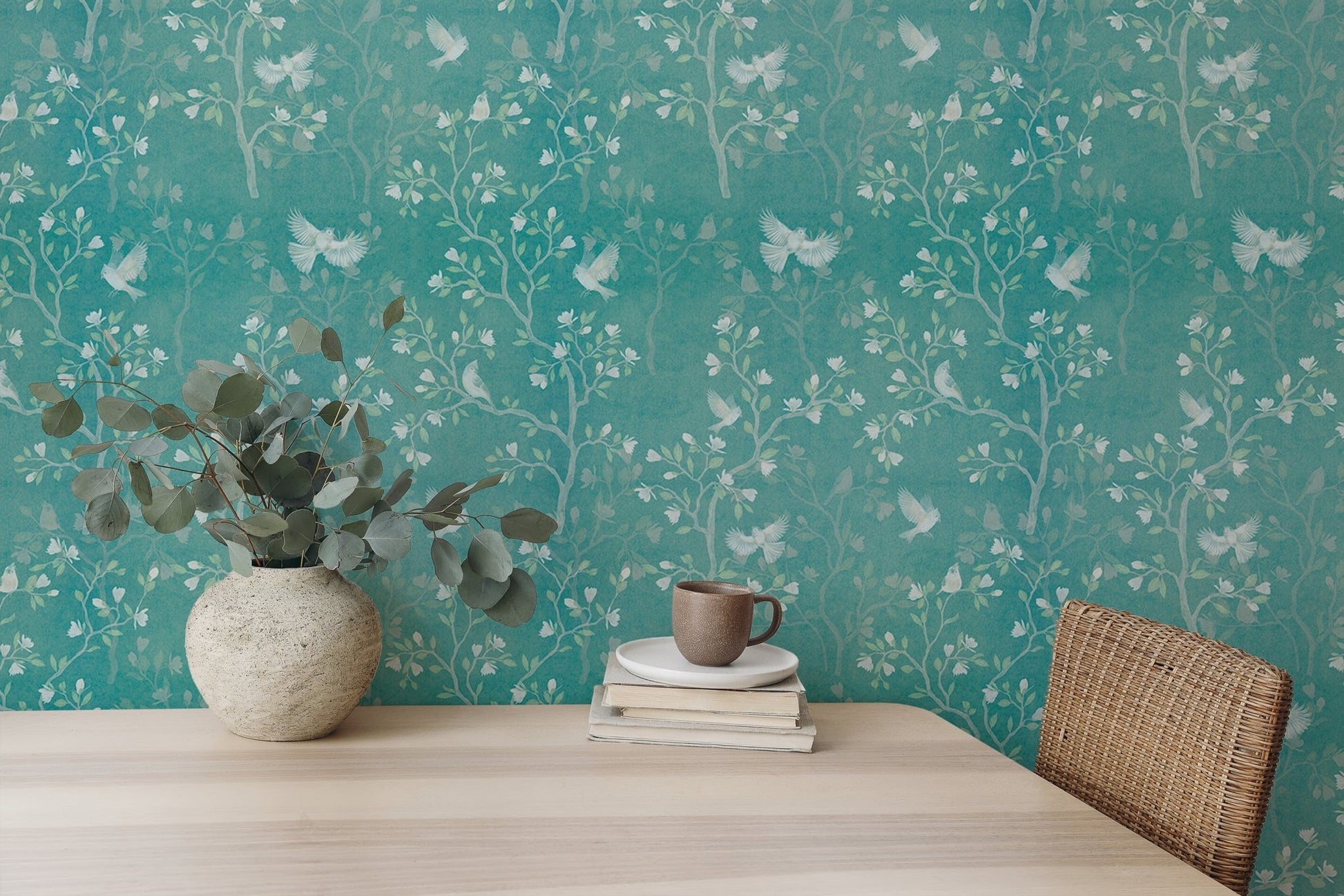 Tree pattern wallpaper on a teal wall behind a light wood desk and plants.
