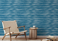 Modern reading area with blue ocean waves wallpaper and a woven chair.
