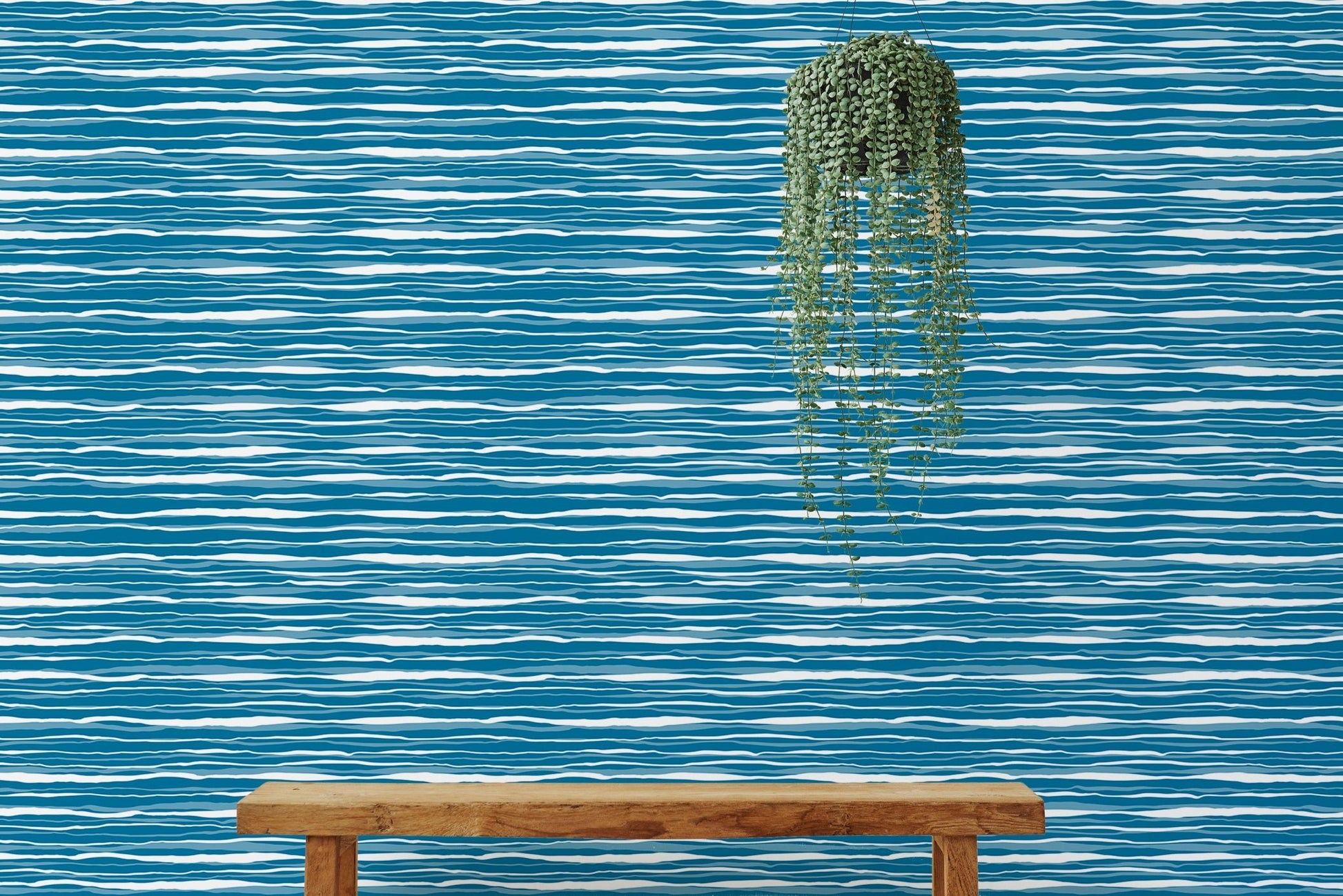 Blue ocean waves wallpaper behind a wooden bench with a hanging green plant.