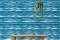 Blue ocean waves wallpaper behind a wooden bench with a hanging green plant.