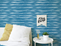 Bedroom wall with blue ocean waves wallpaper behind a white pillow and side table.