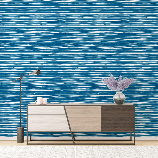 Horizontal blue water stripes wallpaper behind a wooden sideboard and lamp.