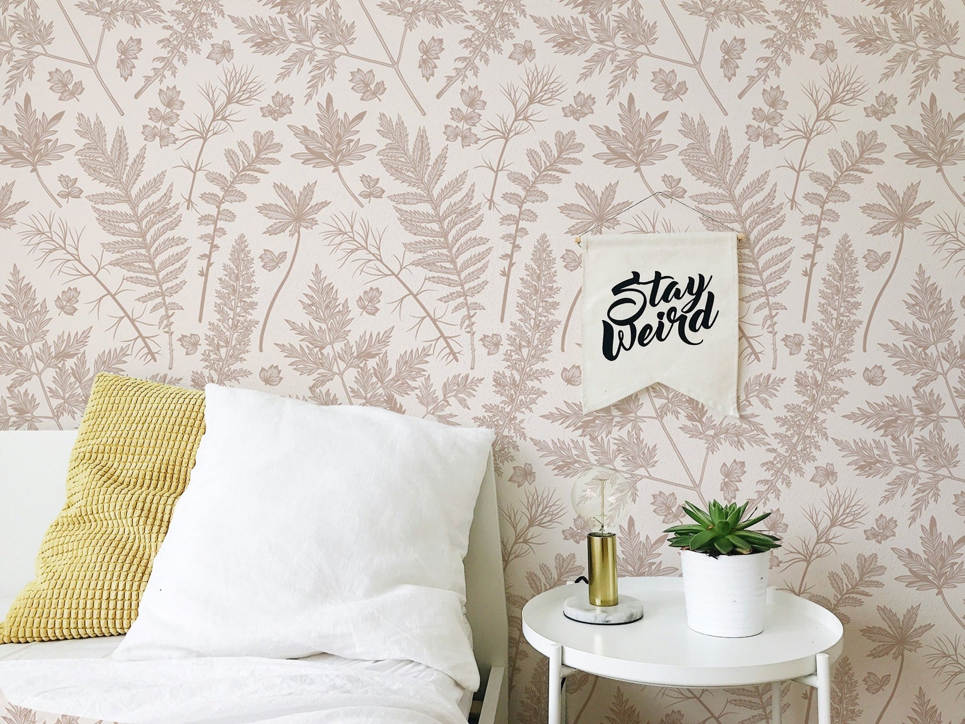 Pastel color leaves wallpaper on a bedroom wall with white pillows and yellow accents.