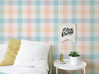 Blue and peach gingham wallpaper in a bedroom behind a white bed.