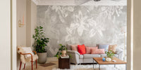 Grey botanical floral wallpaper mural behind a grey sofa in a bright living room.