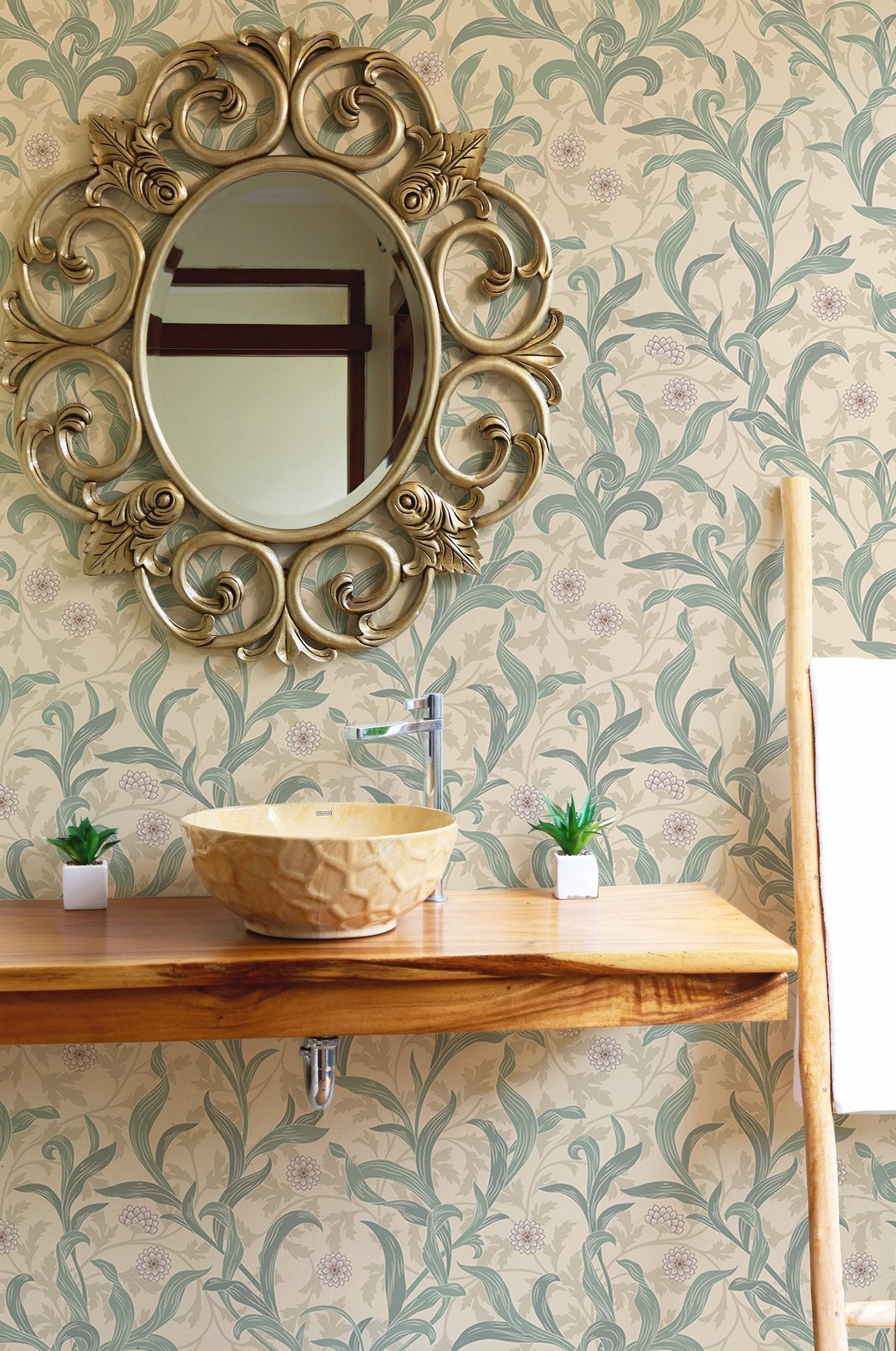 Ornate gold mirror hanging on a vintage flower green leaf wallpaper.