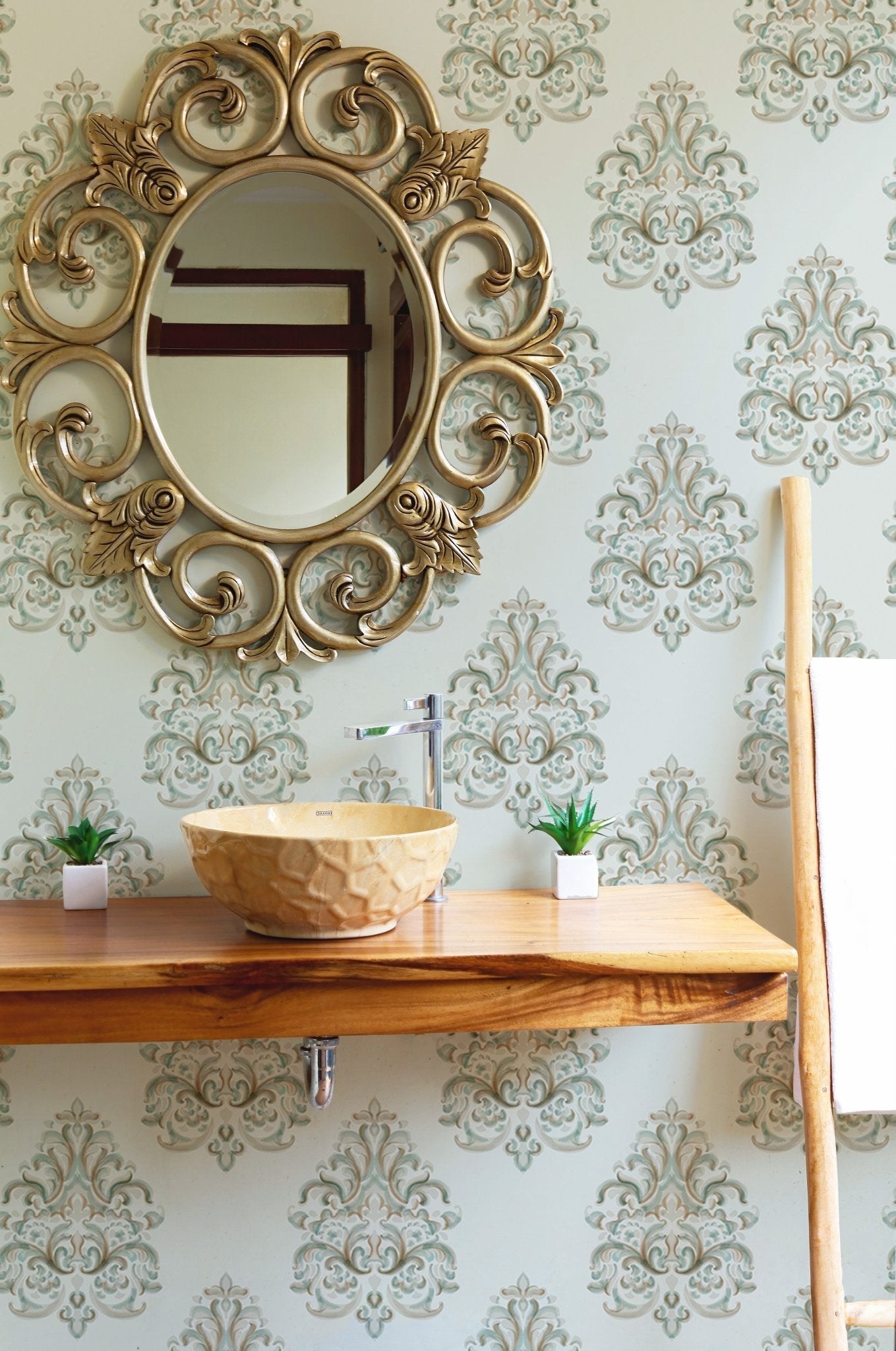 Ornate gold mirror hanging on a green patterned damask wallpaper in a bathroom.