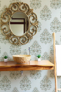 Ornate gold mirror hanging on a green patterned damask wallpaper in a bathroom.