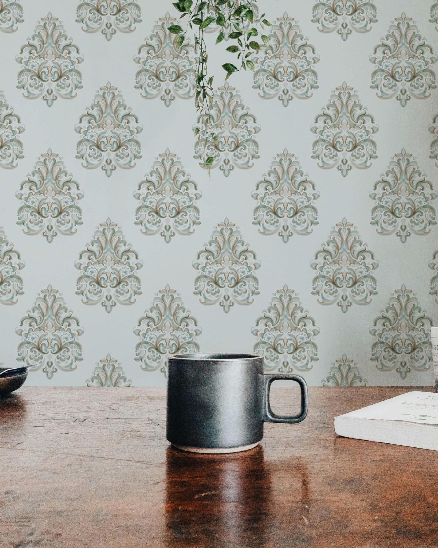 Coffee mug on a wooden table with green damask wallpaper in the background.