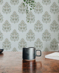 Coffee mug on a wooden table with green damask wallpaper in the background.