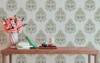 Green damask wallpaper on a study wall with a wooden desk and pink flowers.