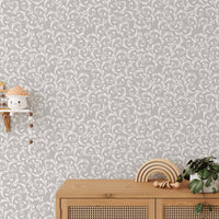 Ornate damask wallpaper pattern behind a wooden sideboard and green plant.