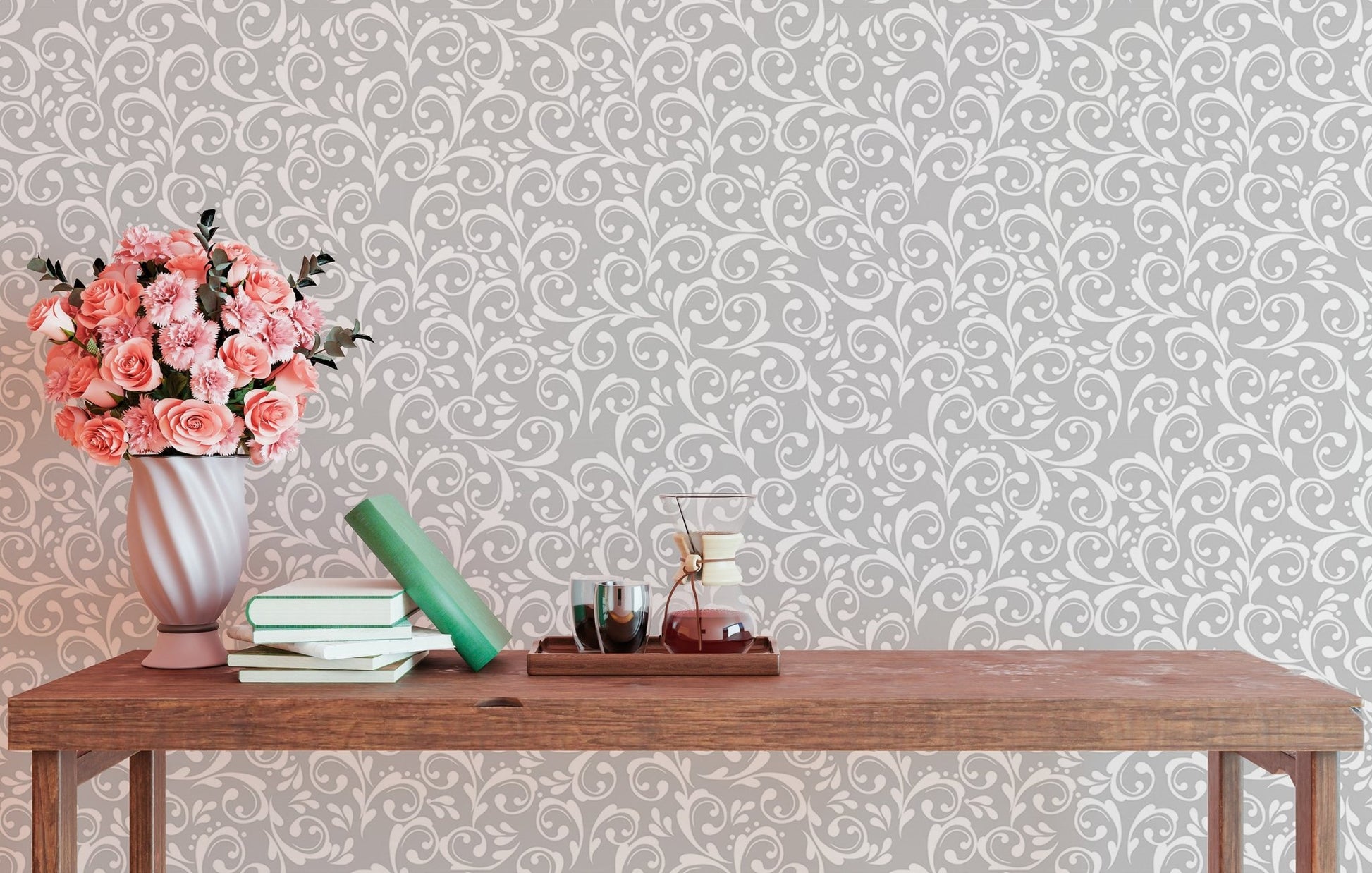 Damask wallpaper behind a wooden table with books and pink flowers.