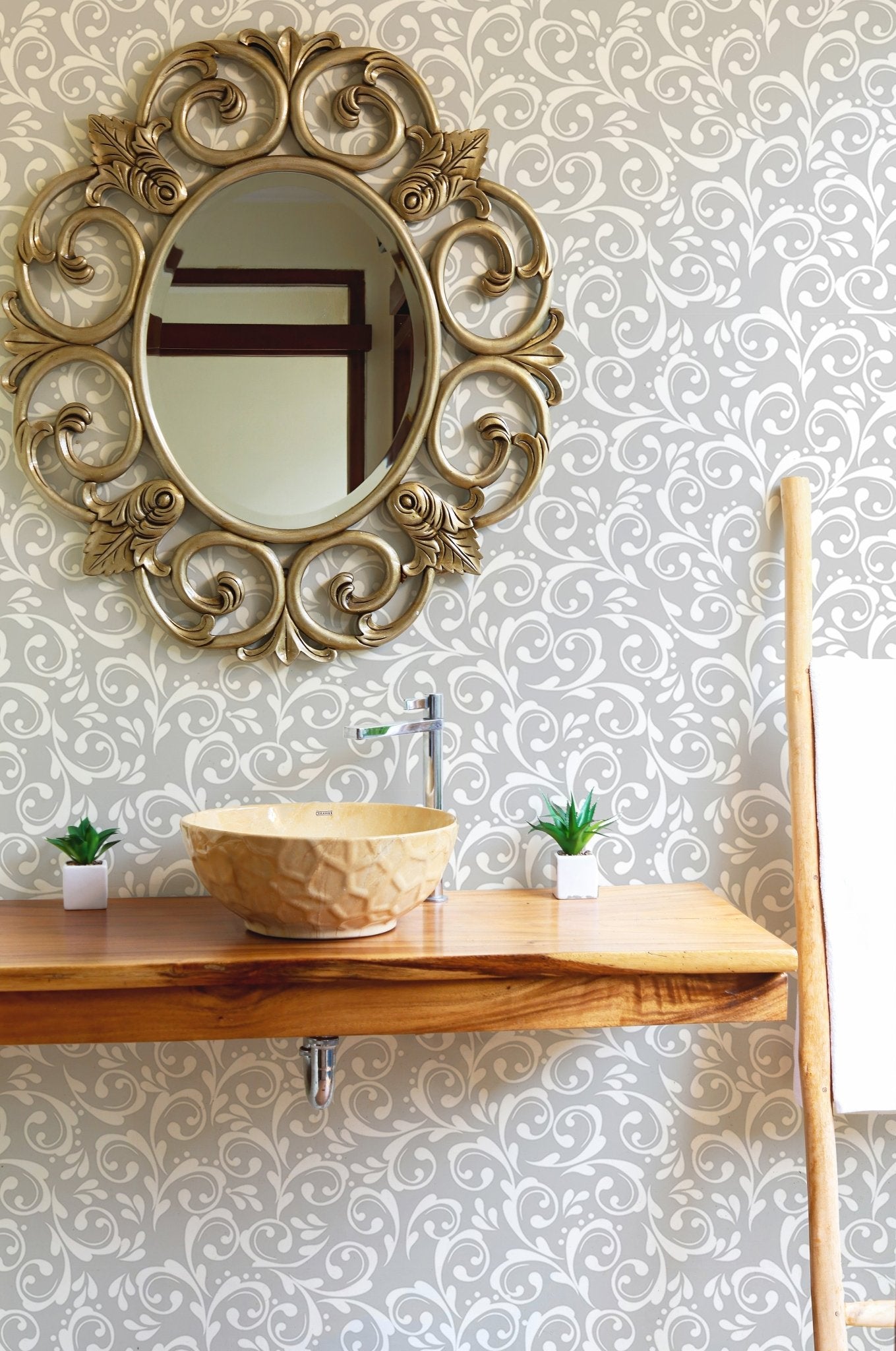 Grey damask wallpaper in a bathroom with a gold mirror and wooden sink.