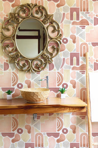Boho wallpaper in bathroom behind a wooden console table with a gold mirror and small plants.