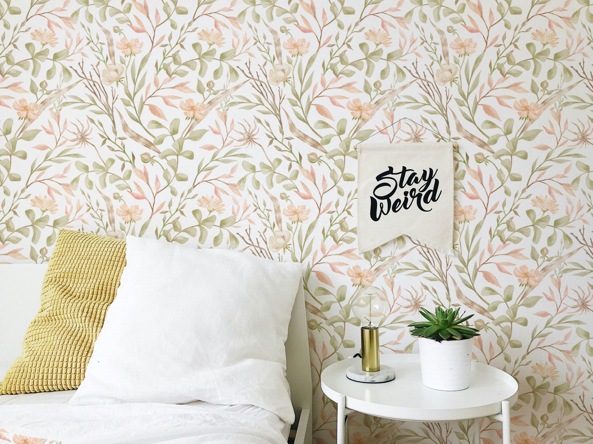 Watercolor green leaf wallpaper in a bedroom corner with a white side table.
