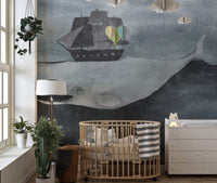 Nursery wall mural with a watercolor whale and pirate ship next to a wooden cot.