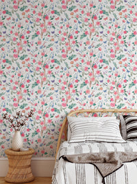 Watercolor rose wallpaper behind a bed with neutral linens and wood side table.