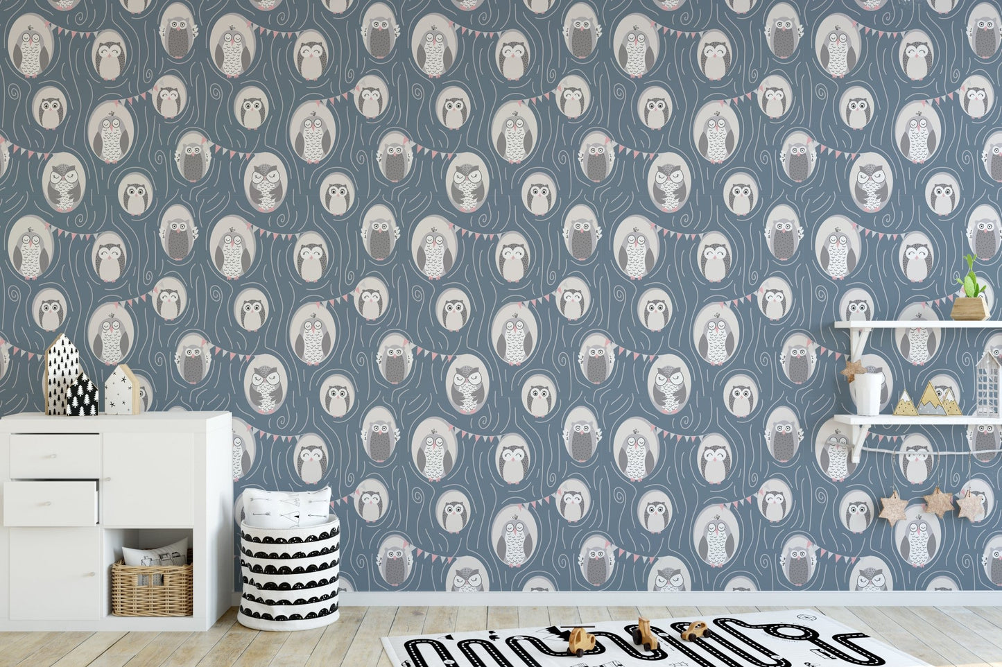 Blue nursery wallpaper with grey owl motifs behind a white wooden crib and play mat.