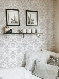 Damask mural in a white bedroom with framed art and a wall shelf.