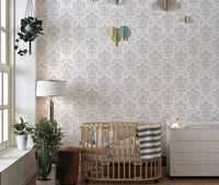 Damask repeat pattern wall mural in a nursery with a wooden crib and green plants.