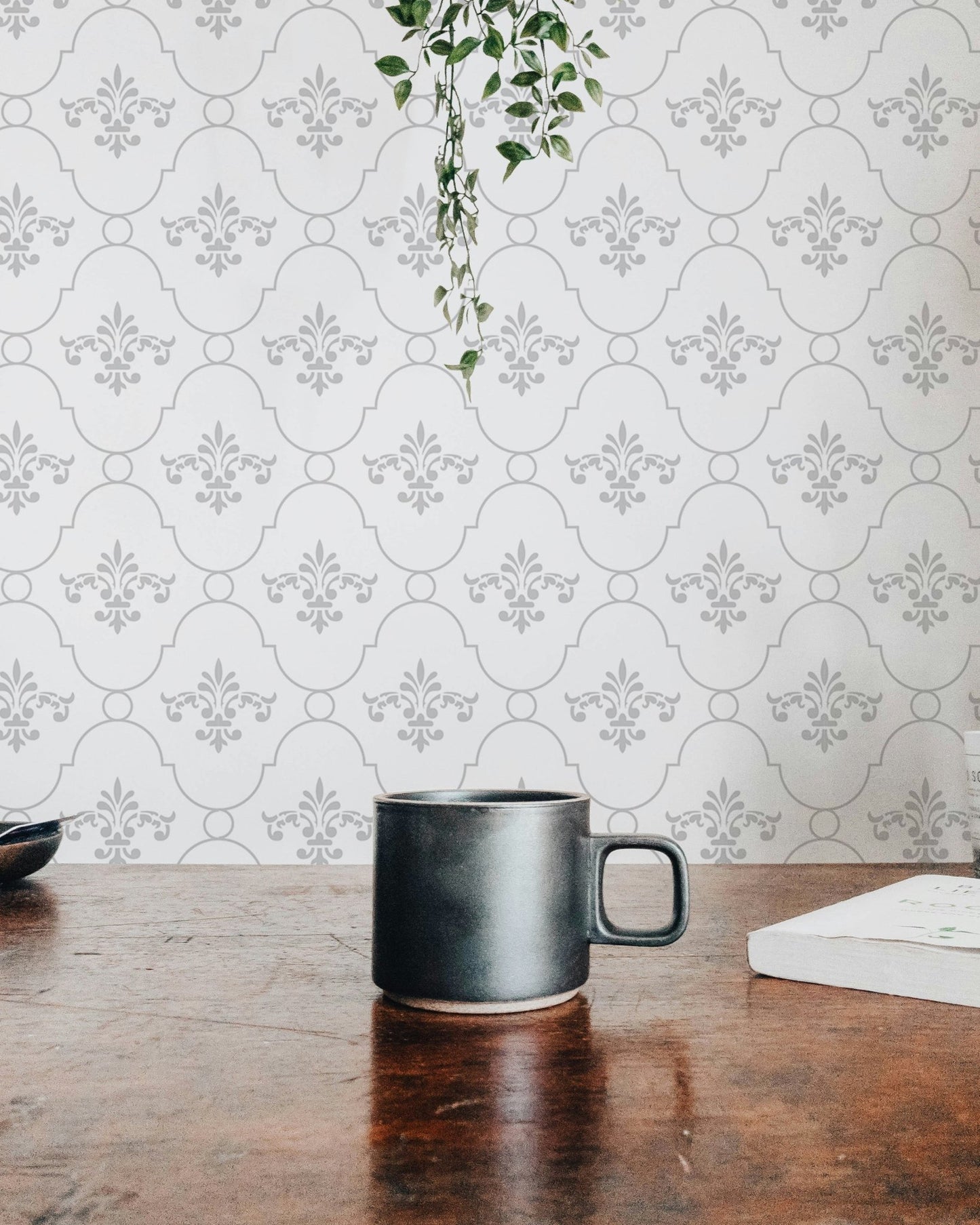 White and grey color vintage look damask wallpaper behind a wooden table and mug.