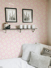 White flowers on pink wallpaper behind a shelf with framed art and candles.