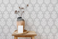 Textured damask wallpaper behind a brown vase on a wooden stool.