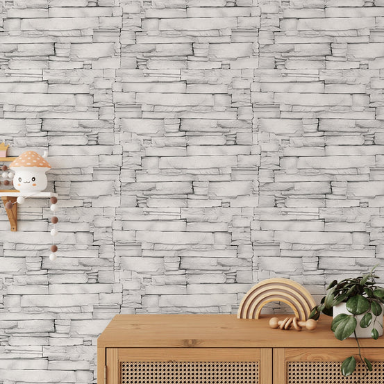 White color limestone masonry wallpaper behind a light wood sideboard with decor.