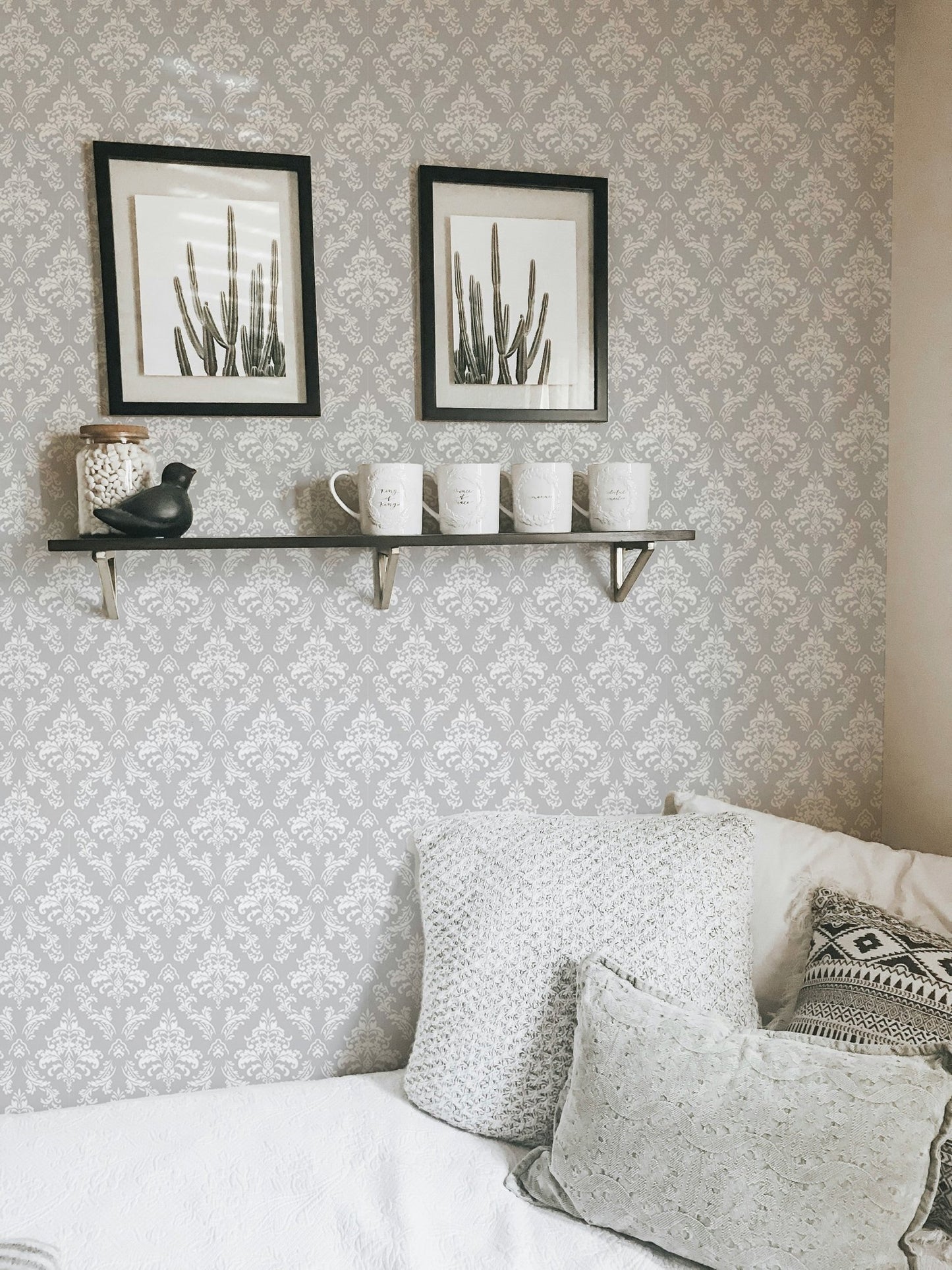 Patterned wallpaper with mini damask shapes behind a white sofa and wall shelves.