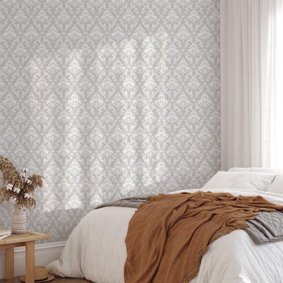 Grey and white damask wallpaper in a bedroom with orange textile accents.