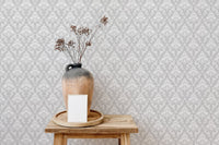 Geometric damask wallpaper behind a ceramic vase and dried flowers on a wood stool.