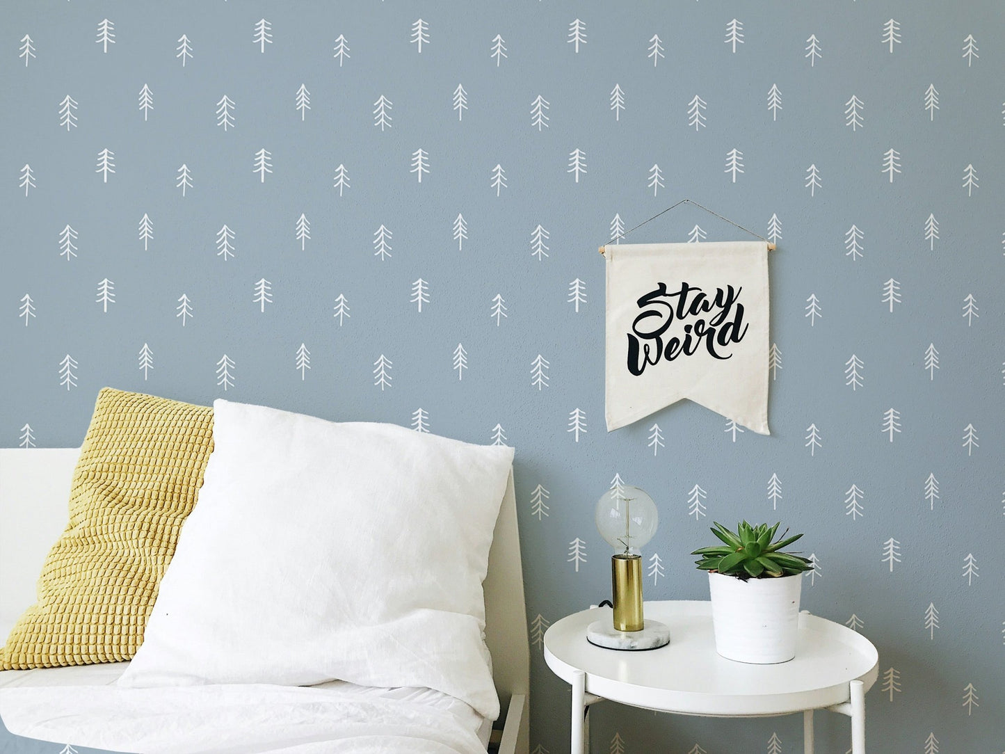 Modern tree wallpaper in bedroom behind white pillows and small plant.